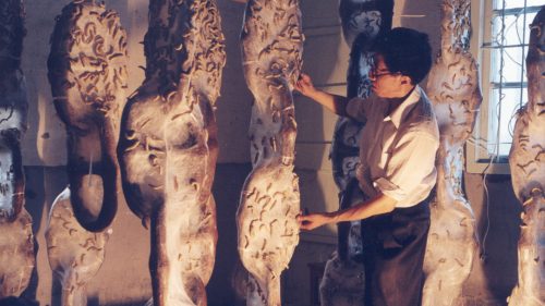 A man gestures to silk worm covered hanging chains